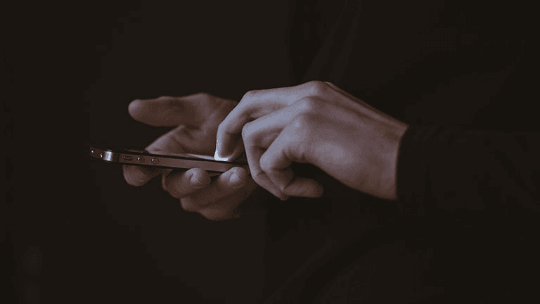 Homme tenant un cellulaire entre ses mains dans le noir